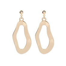 Détail de boucles d'oreilles vagues géométriques irrégulières en métal doré poli