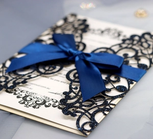 Detail of navy laser-cut wedding invitation with glitter sleeve and blue satin ribbon