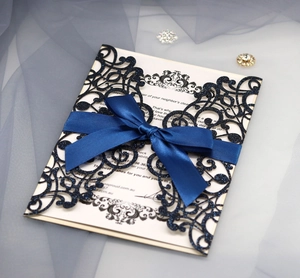 Close-up of navy blue glitter laser-cut wedding invitation with elegant satin bow