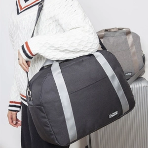 Detail view of a large black travel bag with gray reinforced straps shown in a travel scene