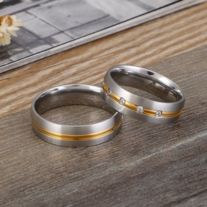 Matte silver and gold titanium steel couple rings with cubic zirconia on wood surface