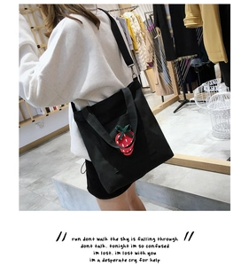 Detail shot of a black canvas tote bag featuring an embroidered red strawberry pattern