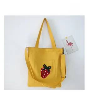 Close-up of yellow canvas tote bag featuring strawberry embroidery and dual straps