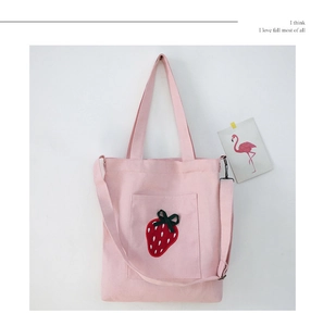 Close-up of pink canvas bag with strawberry embroidery, dual handles and long strap