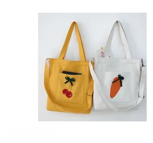 Detail view of two canvas bags featuring cherry and carrot embroidery with adjustable straps