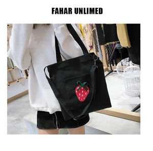 Detail of black canvas tote bag featuring embroidered red strawberry and adjustable strap