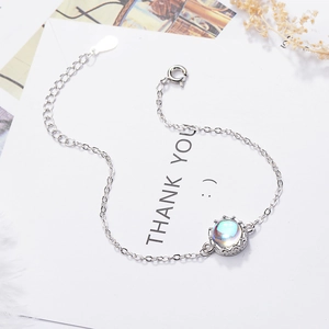 Elegant silver crown bracelet with shimmering moonstone pendant on a white floral card