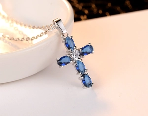 Macro shot of silver cross necklace with oval blue sapphires and center clear zircon
