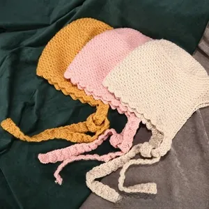 Close-up of hand-knitted baby hats with wavy crochet edges and long ties in soft yarn
