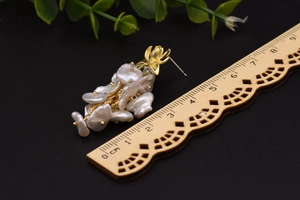 Dettaglio macro di orecchini a nappa in perle barocche da 5cm con perni floreali dorati