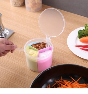 Close-up of a circular multi-compartment seasoning box with small spoons on a wooden table