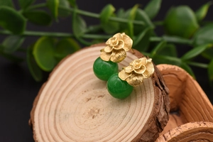 Detailed close-up of golden metal rose earrings with vintage green jade beads on wood