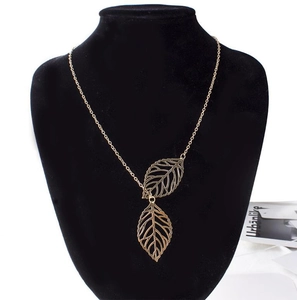 Close-up of golden necklace with two hollow leaf pendants on a black velvet mannequin