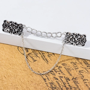 Dettaglio di fermagli vintage in argento per cardigan con incisione floreale e catena