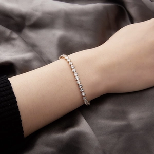 Close-up of a gold tennis bracelet with clear crystals and a heart charm on a wrist