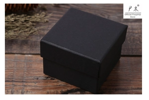 Gros plan d'une boîte cadeau carrée en carton noir mat sur une surface en bois sombre