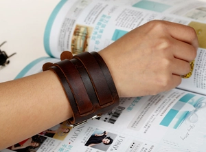 Detail of deep brown wide leather wristband featuring retro texture and silver buckles