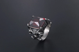 Macro shot of gothic titanium steel ring with red faceted stone and fleur-de-lis patterns