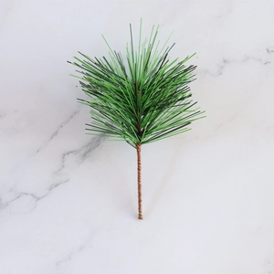 Close-up of artificial green pine needles with brown stems on white marble background
