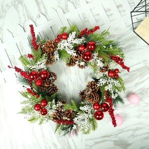 Christmas wreath with PE pine needles, red berries, cones, and ornaments on marble background
