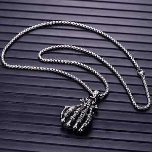 Detail of gothic silver skeleton claw pendant and box chain on a dark textured surface