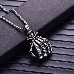 Detailed macro shot of vintage stainless steel ghost hand skull pendant on black surface