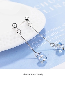 Close-up of long silver earrings with light blue crystal cube pendants on white plate