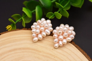 Detailed close-up of pearl cluster earrings on a wooden base with green leaves