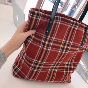 Macro detail of red plaid canvas tote bag with black leather straps and gold rivets