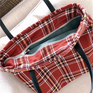 Detail view of red and white plaid tote bag showing dark green lining and inner zipper pocket