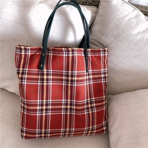Detail of red tartan tote bag with dark green shoulder strap and gold rivets on a sofa