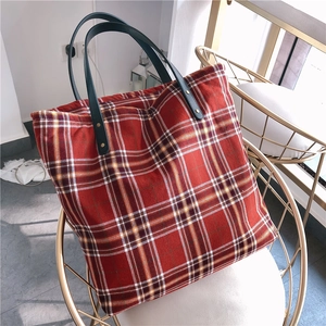 Detailed close-up of rivet reinforcement and green handles on red plaid tote bag