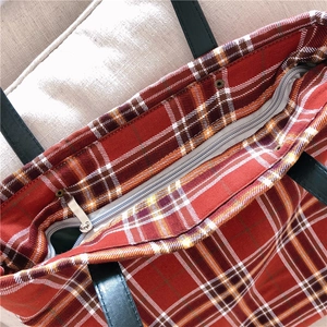 Detail of red plaid tote bag with silver zipper closure and black leather straps