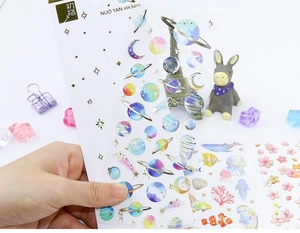 Close-up of translucent gold-stamped stickers featuring starry sky and dolphin designs