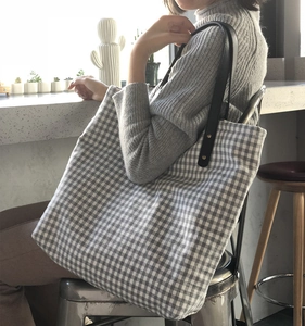 Detail of grey gingham tote bag with black leather straps and gold rivet fasteners