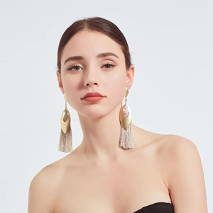 Close-up of elegant gold hollow metal earrings with cream white tassel fringe details