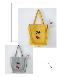 Detail of canvas tote bags with cherry embroidery, featuring adjustable straps and pockets