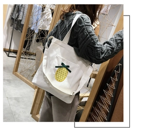 Detail of a white canvas tote bag featuring a cute yellow embroidered pineapple design
