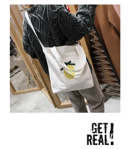 Detail of cute pineapple embroidery on cream canvas tote bag with Get Real text