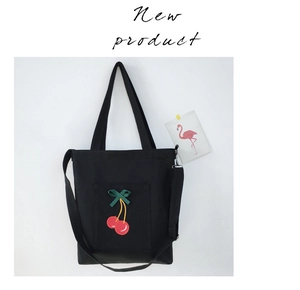 Detail of black canvas tote bag featuring red cherry embroidery and a green ribbon bow