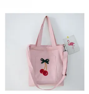 Detailed embroidery of red cherries and dark green bow on a pink canvas tote bag