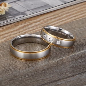 Frosted gold-edged stainless steel couple rings with cubic zirconia on wooden surface
