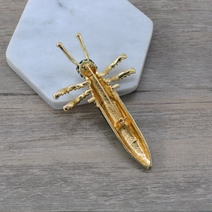 Detail showing the secure metal pin clasp and back structure of a gold insect brooch