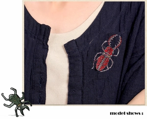 Vue détaillée d'une luxueuse broche scarabée en strass rouges sur une chemise en lin bleu
