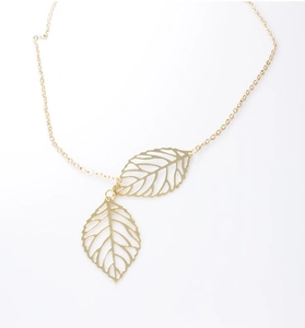 Macro shot of gold double leaf pendants on a delicate chain necklace with镂空 texture