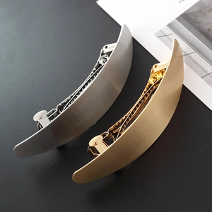 Detailed view of curved gold and silver metallic oval hair clips with brushed finish texture