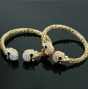 Detail of open cuff bracelets featuring crystal-studded skulls on polished gold metal