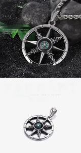 Detailed view of punk style nautical compass pendant on black stones and green leaves