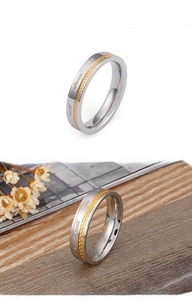 Détail d'une bague bicolore en acier avec texture grillagée dorée et gravure romantique