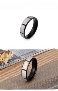Detail of black and silver stainless steel ring with brushed texture and geometric grooves